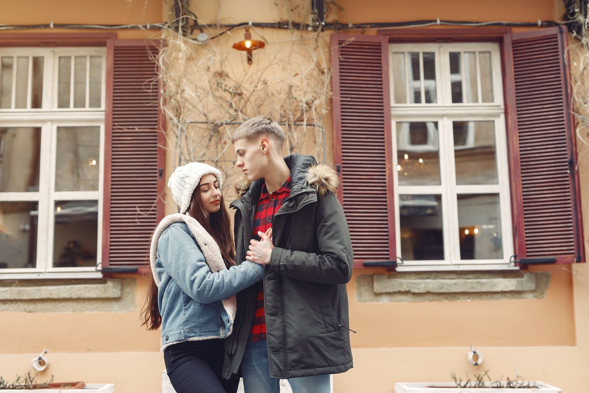 Zimowe randki w plenerze: sposoby na mróz i dobrą zabawę Para na zimowej randce w mieście trzyma się za ręce przed kamienicą
