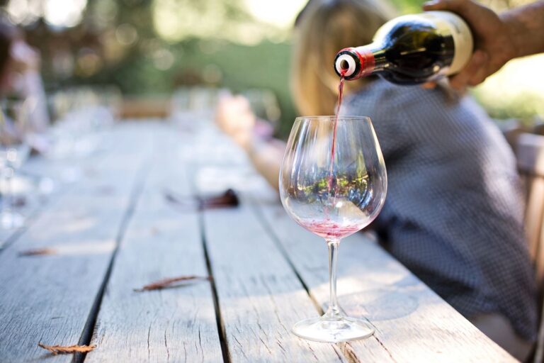 Dłoń nalewająca czerwone wino do kieliszka na stole w plenerze